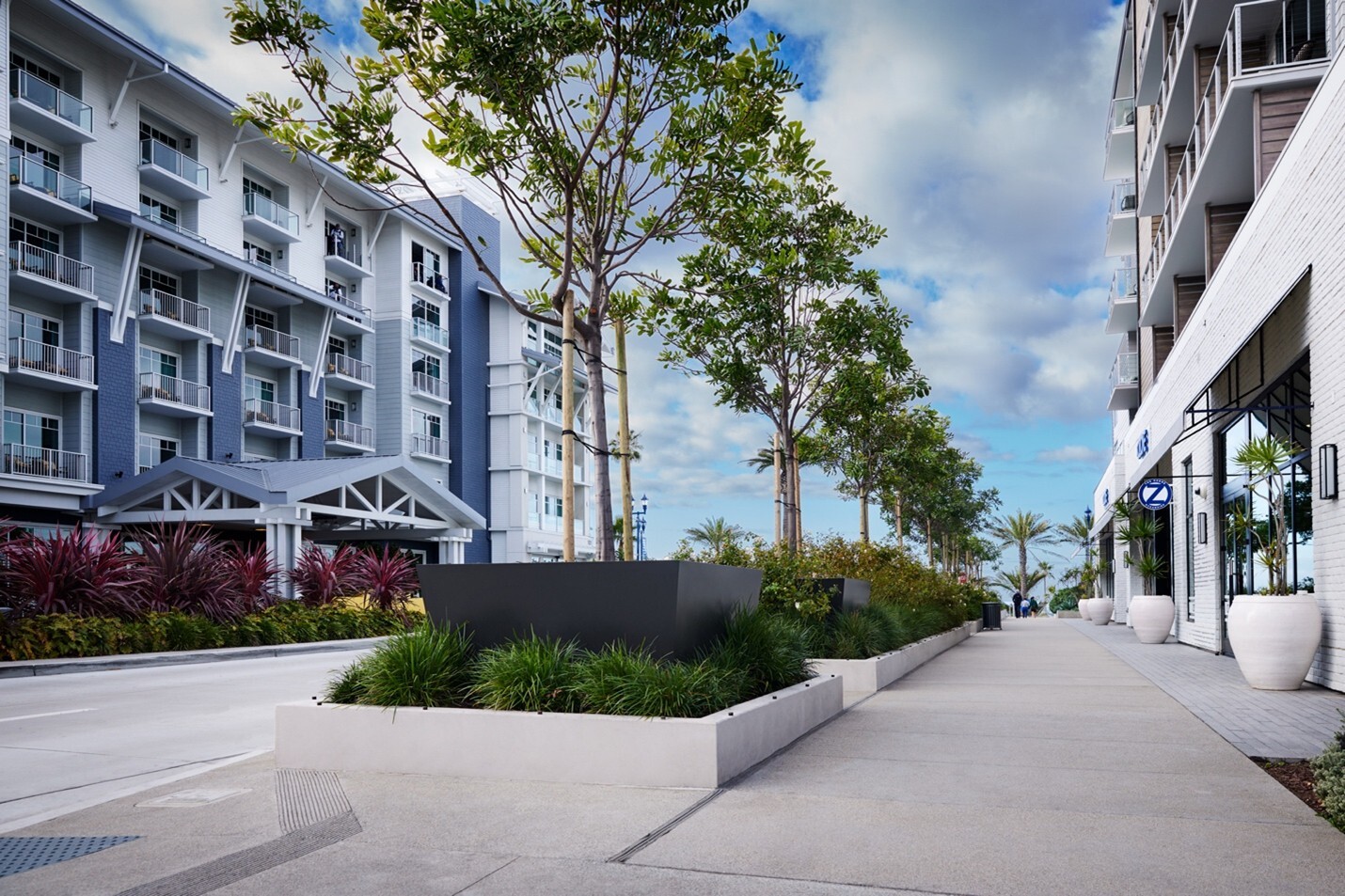 Sidewalk with large commercial planters in center and round planters flanking building entrances